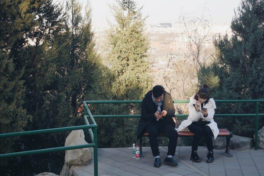 couple on phones on park bench busyness is destroying your marriage