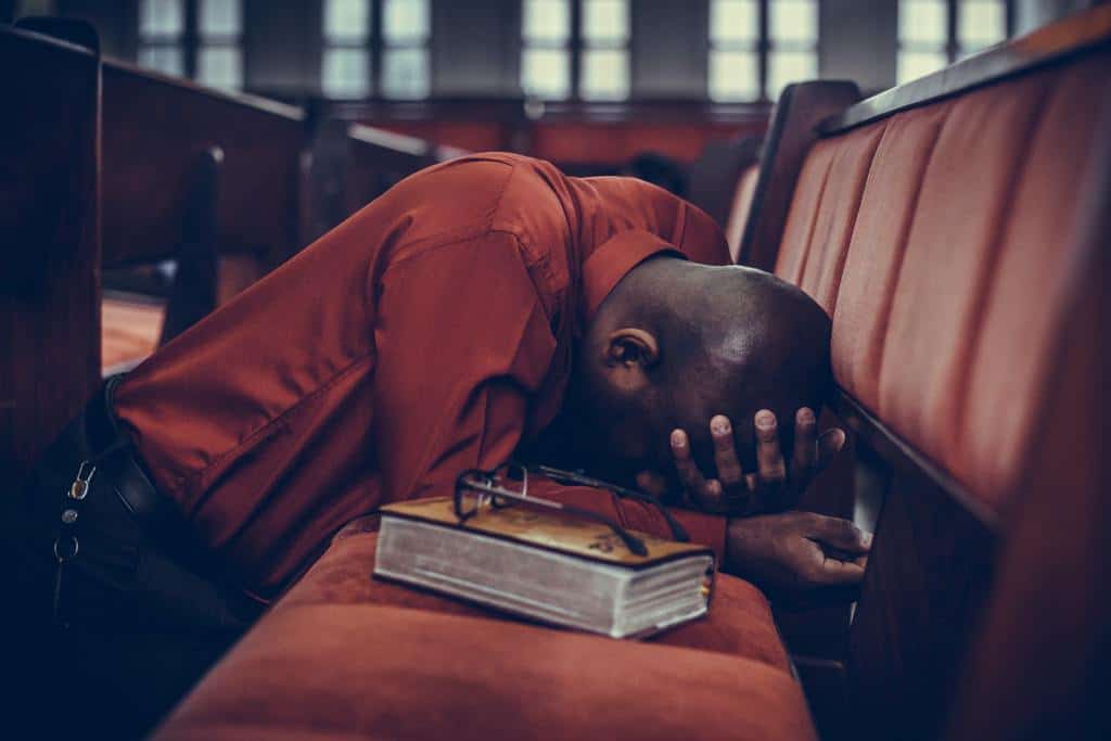 man praying with bible on pew